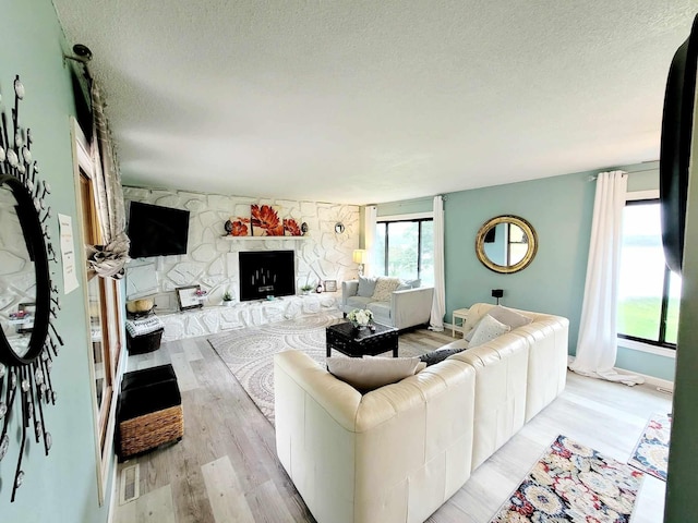 living area with a textured ceiling, a stone fireplace, and light wood-style flooring