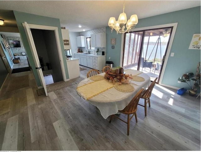 dining area featuring light wood-style flooring, baseboards, a chandelier, and a textured ceiling