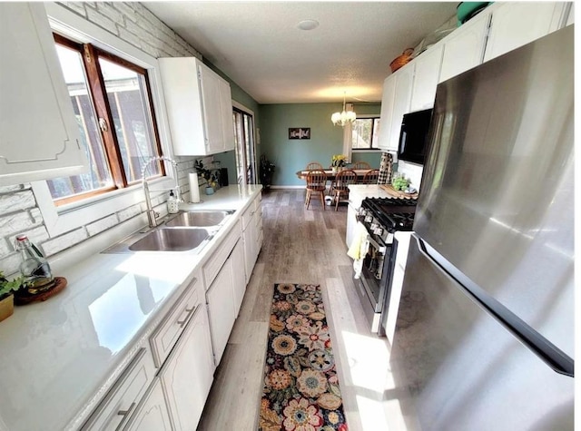 kitchen with white cabinets, hanging light fixtures, stainless steel appliances, light countertops, and light wood-type flooring