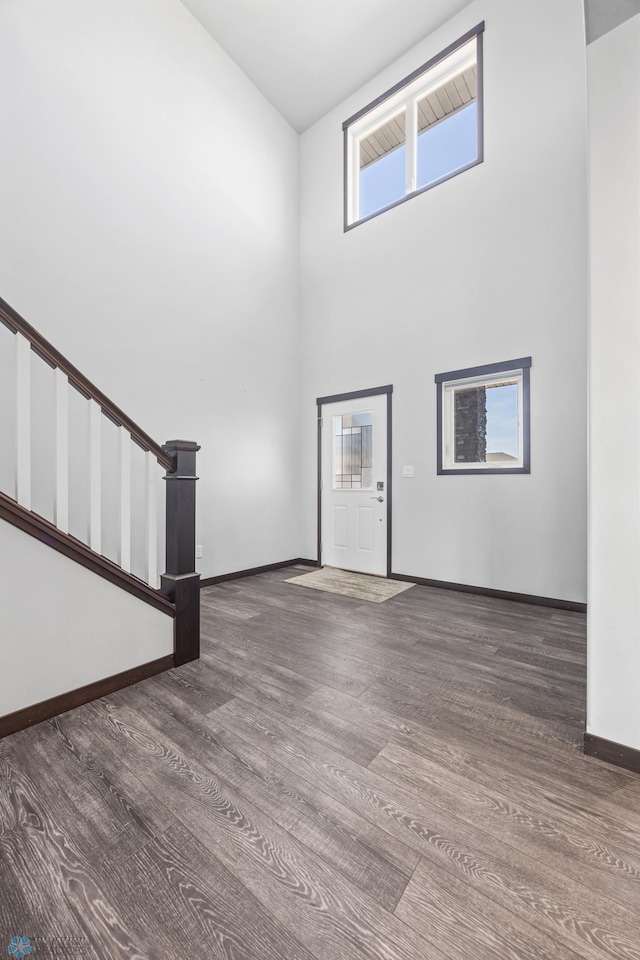 unfurnished living room with baseboards, stairs, a high ceiling, and wood finished floors