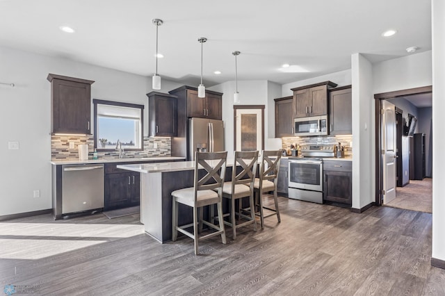 kitchen with dark wood-style flooring, stainless steel appliances, light countertops, dark brown cabinets, and a kitchen bar