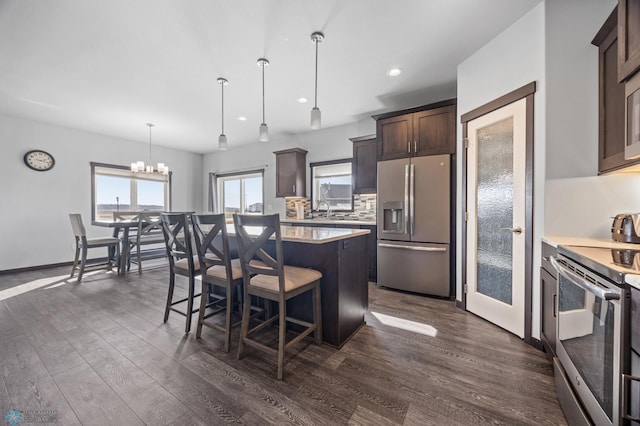 kitchen with dark wood finished floors, decorative backsplash, stainless steel appliances, dark brown cabinets, and light countertops