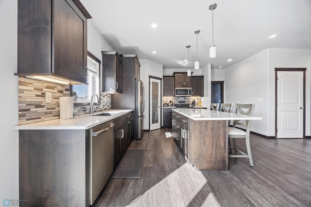 kitchen with a kitchen island, a sink, a kitchen breakfast bar, dark brown cabinets, and appliances with stainless steel finishes