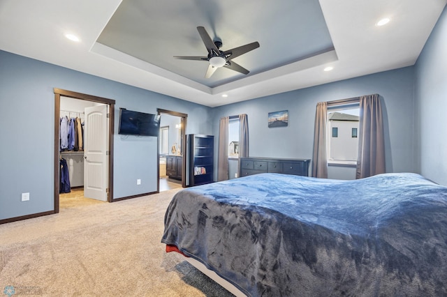 carpeted bedroom with a spacious closet, a tray ceiling, recessed lighting, and baseboards