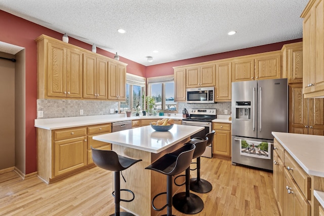 kitchen with a center island, light wood finished floors, a breakfast bar area, stainless steel appliances, and light countertops