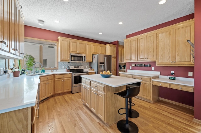 kitchen with appliances with stainless steel finishes, a kitchen breakfast bar, a center island, light countertops, and a sink