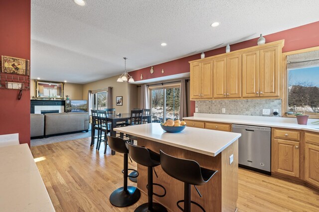 kitchen with light countertops, hanging light fixtures, stainless steel dishwasher, open floor plan, and light wood-type flooring