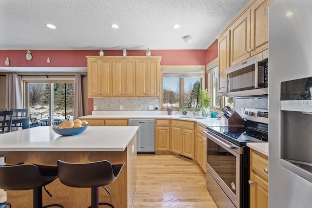 kitchen with stainless steel appliances, a breakfast bar, a kitchen island, light countertops, and light brown cabinetry