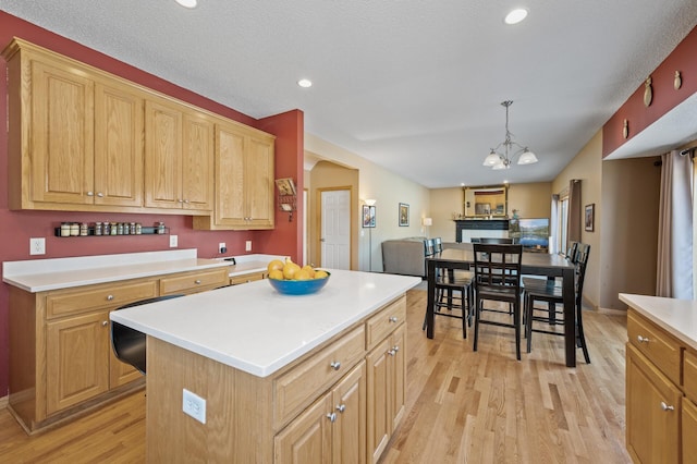 kitchen featuring light wood finished floors, arched walkways, a kitchen island, decorative light fixtures, and light countertops