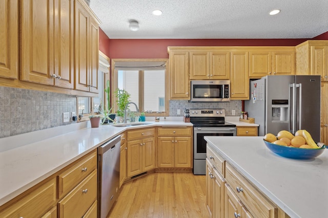 kitchen with light wood finished floors, light countertops, appliances with stainless steel finishes, and a sink