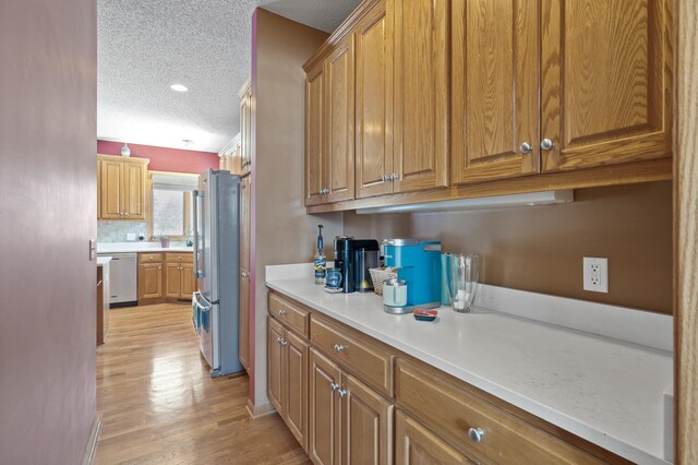 kitchen featuring light wood finished floors, appliances with stainless steel finishes, brown cabinets, light countertops, and a textured ceiling