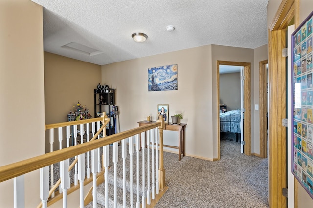 corridor featuring attic access, carpet, a textured ceiling, and an upstairs landing