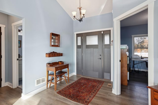 entrance foyer with a notable chandelier, lofted ceiling, visible vents, wood finished floors, and baseboards