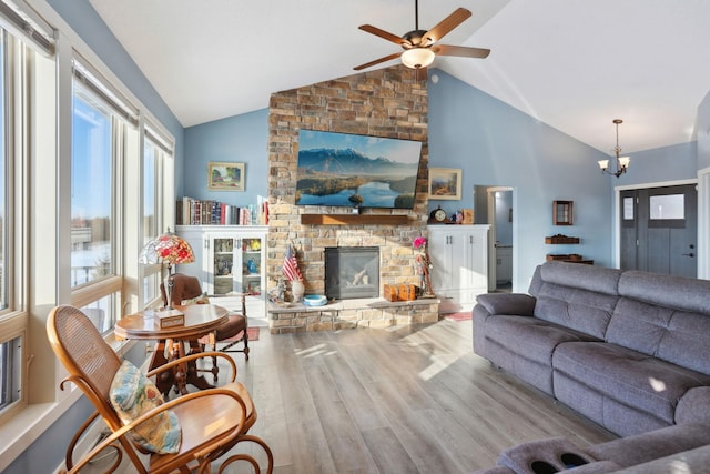 living room featuring high vaulted ceiling, ceiling fan with notable chandelier, wood finished floors, and a stone fireplace