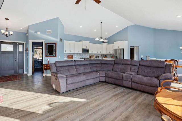 living room with high vaulted ceiling, light wood-type flooring, visible vents, and ceiling fan with notable chandelier