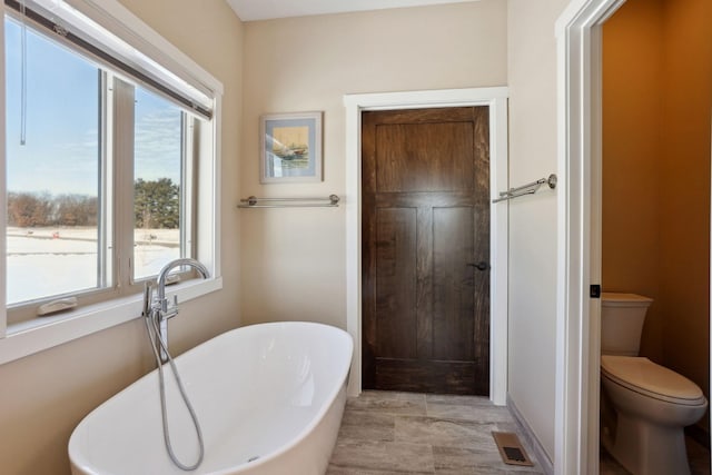 bathroom with a freestanding tub, visible vents, and toilet