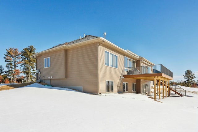 snow covered back of property featuring stairway and a deck