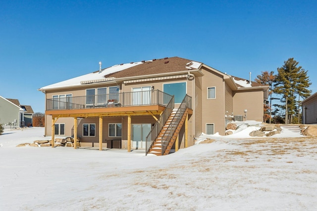 snow covered rear of property with stairs and a wooden deck