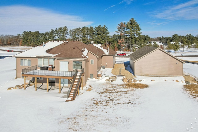 snow covered back of property with stairway and a wooden deck