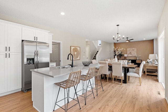 kitchen with a sink, white cabinets, light countertops, an island with sink, and stainless steel fridge