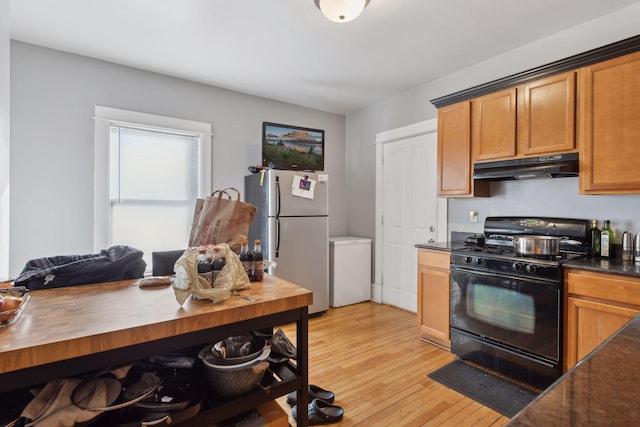 kitchen featuring black range with gas cooktop, under cabinet range hood, light wood-style floors, freestanding refrigerator, and dark countertops