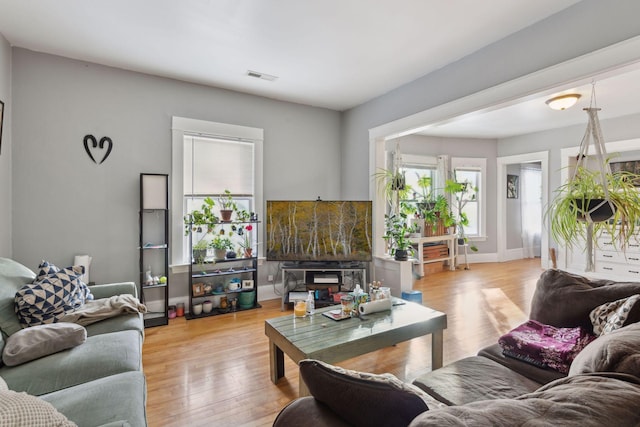 living room with light wood finished floors, visible vents, and baseboards