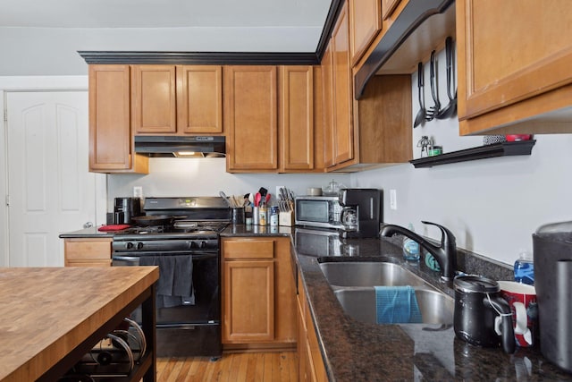 kitchen with under cabinet range hood, a sink, dark stone counters, stainless steel microwave, and gas stove