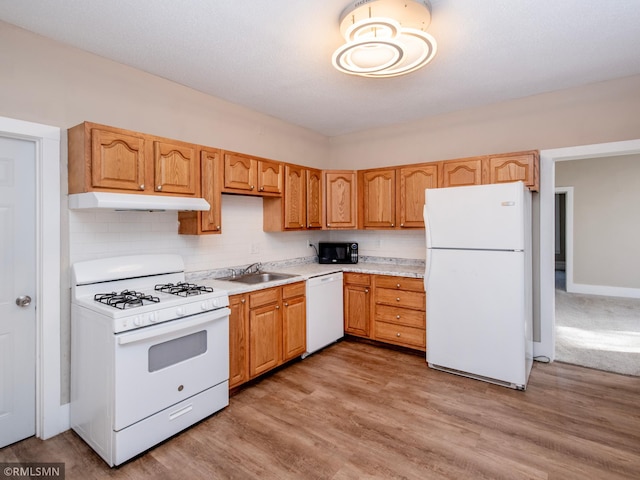 kitchen featuring white appliances, light countertops, light wood-type flooring, under cabinet range hood, and a sink