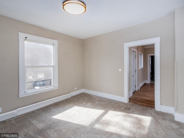 carpeted empty room featuring a baseboard heating unit and baseboards