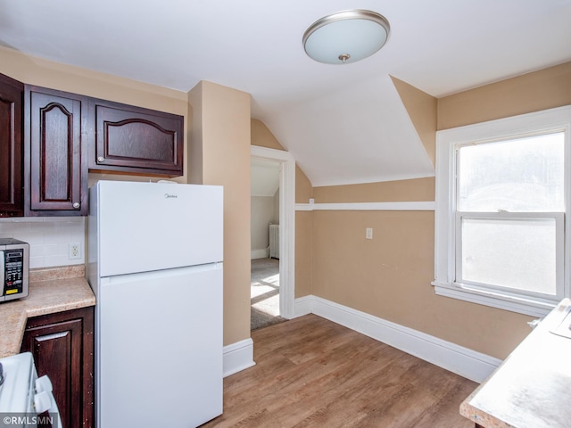 kitchen featuring light countertops, decorative backsplash, freestanding refrigerator, and dark brown cabinetry