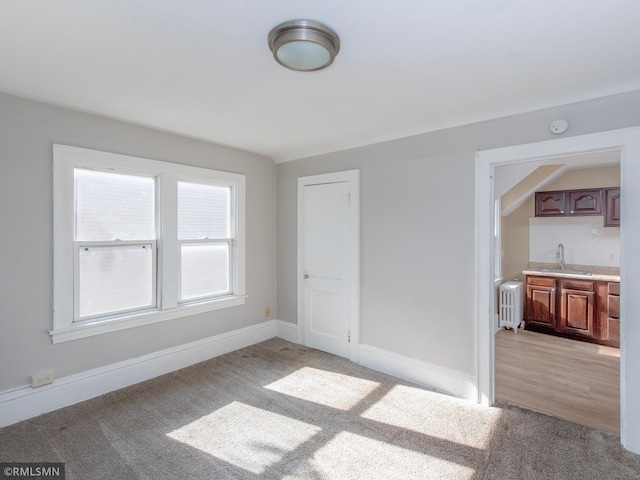 empty room featuring light carpet, radiator heating unit, a sink, and baseboards