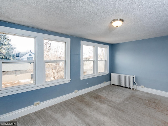 spare room with baseboards, light colored carpet, a textured ceiling, and radiator heating unit