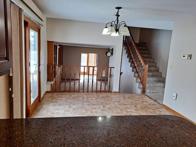 foyer featuring stairs, stone finish flooring, a textured ceiling, and a notable chandelier