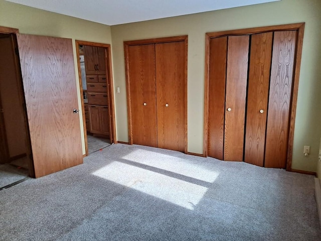 unfurnished bedroom with light carpet, baseboards, and multiple closets