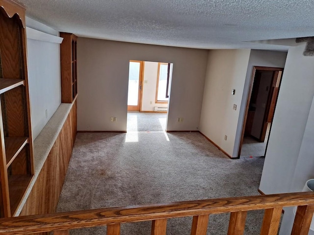 unfurnished room featuring light carpet, a textured ceiling, and baseboards