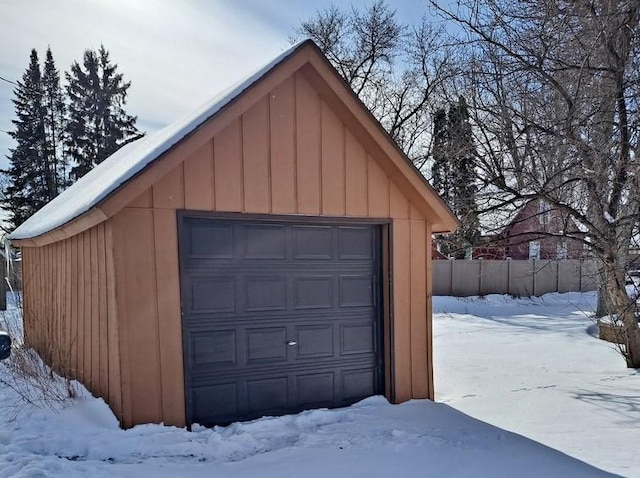 snow covered garage with a detached garage and fence