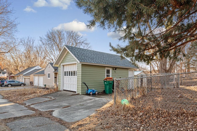 view of property exterior with roof with shingles, a detached garage, fence, and an outdoor structure