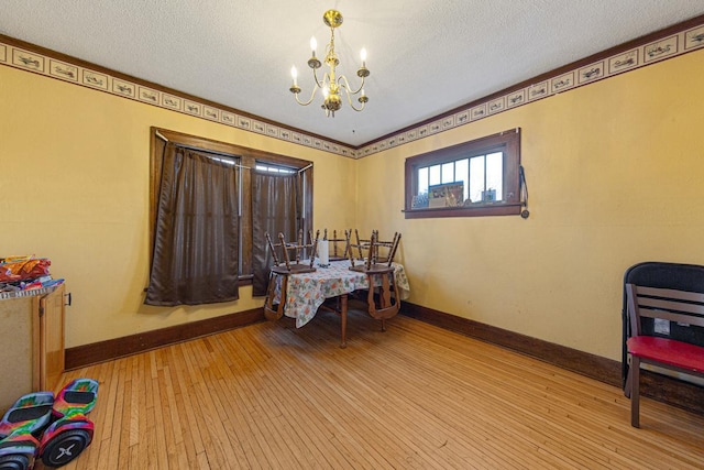 dining area with light wood-style floors, a textured ceiling, baseboards, and a notable chandelier