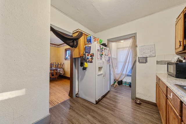 kitchen with white refrigerator with ice dispenser, brown cabinets, dark wood-style flooring, light countertops, and black microwave