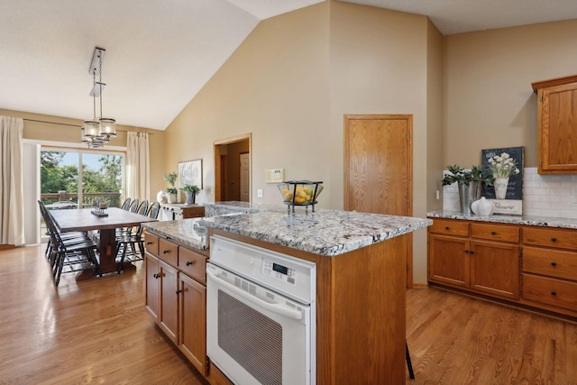 kitchen featuring a center island, light wood-style floors, white oven, brown cabinets, and decorative light fixtures