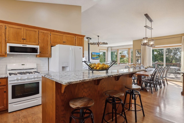 kitchen featuring a breakfast bar area, white appliances, backsplash, brown cabinets, and pendant lighting