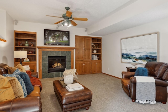 carpeted living area with built in shelves, baseboards, a ceiling fan, and a tile fireplace