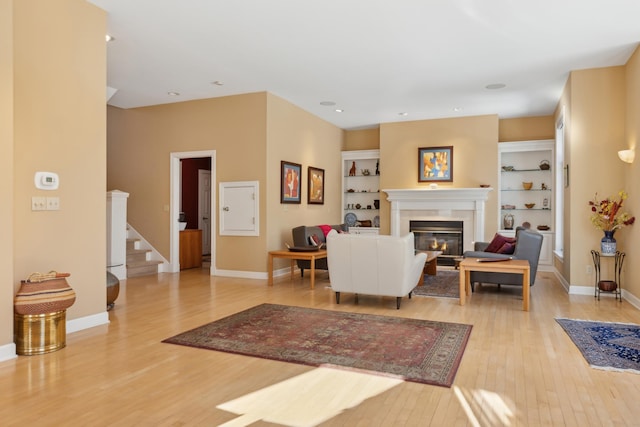 living room with light wood-type flooring, baseboards, stairway, and a glass covered fireplace