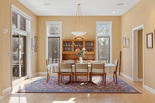 dining room with baseboards, a high ceiling, light wood-type flooring, and a healthy amount of sunlight