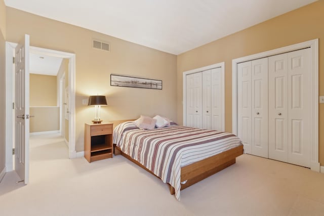 bedroom with baseboards, visible vents, two closets, and light colored carpet