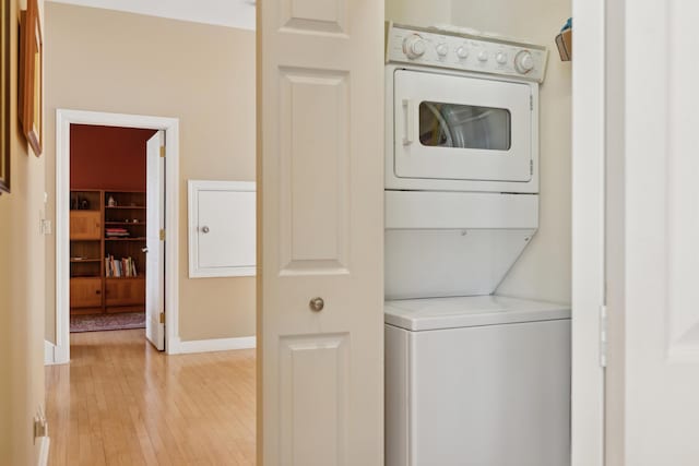 washroom with stacked washer and dryer, laundry area, light wood-style flooring, and baseboards