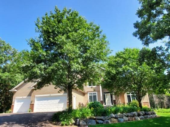 view of property hidden behind natural elements with driveway and an attached garage