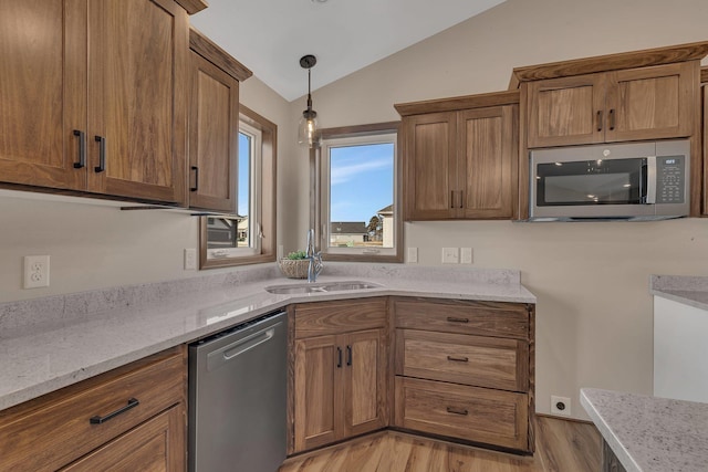 kitchen featuring light stone counters, brown cabinetry, a sink, vaulted ceiling, and appliances with stainless steel finishes