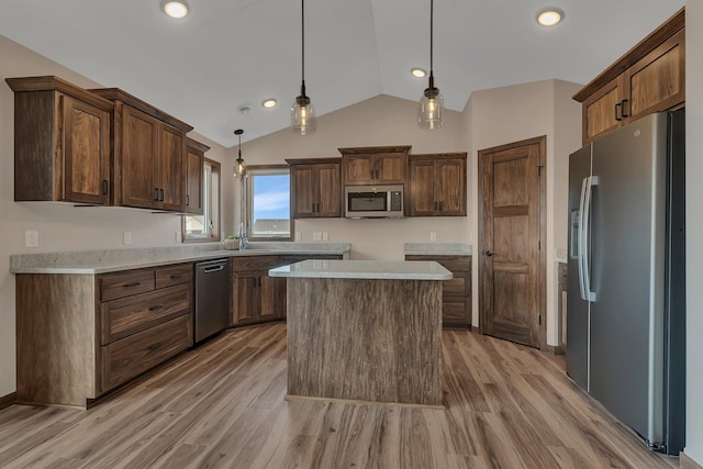 kitchen featuring light wood-type flooring, decorative light fixtures, a sink, appliances with stainless steel finishes, and lofted ceiling