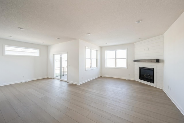 unfurnished living room featuring a textured ceiling, light wood finished floors, a fireplace, and baseboards